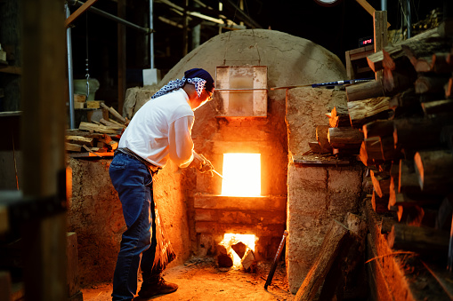 Senior pottery craftsmen stoking the fire in his large kiln