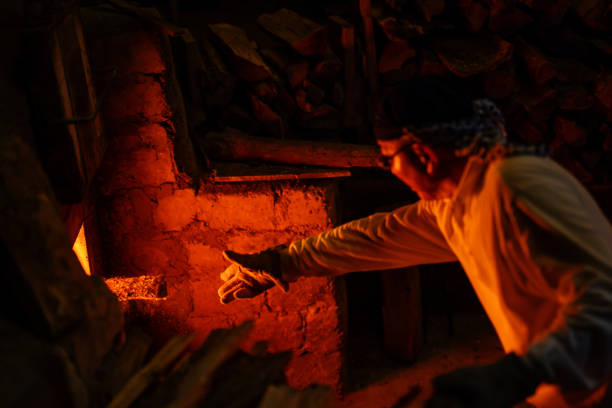 istock Senior pottery craftsmen adding firewood to his large kiln 1282292506