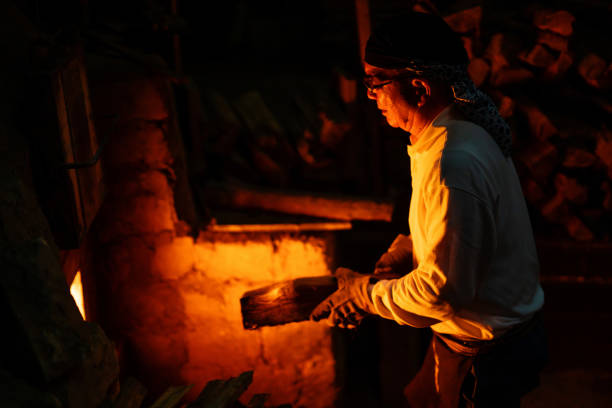 alte töpferhandwerker fügen brennholz zu seinem großen ofen hinzu - kiln ceramic ceramics fire stock-fotos und bilder