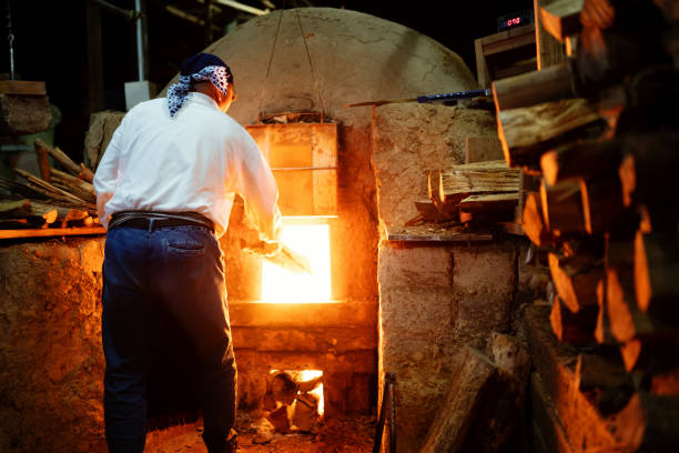 istock Senior pottery craftsmen adding firewood to his large kiln 1282292526