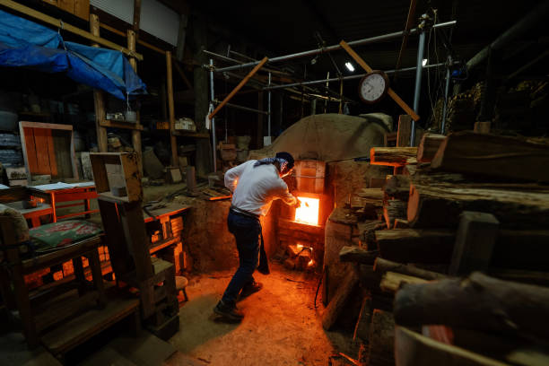 alte töpferhandwerker fügen brennholz zu seinem großen ofen hinzu - kiln ceramic ceramics fire stock-fotos und bilder