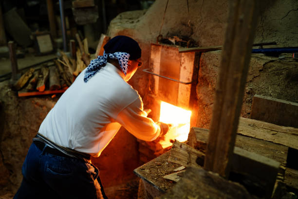 Molten glass on a blowpipe is inside of an open furnace, glass blowing workshop