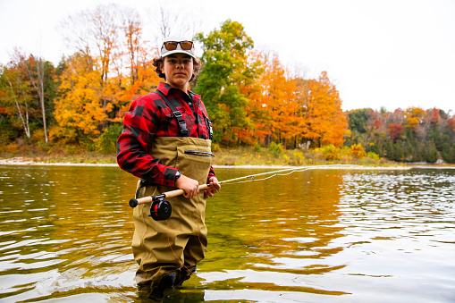 Fly-fishing on a beautiful Autumn day. A young fly fisherman in a river during the fall.