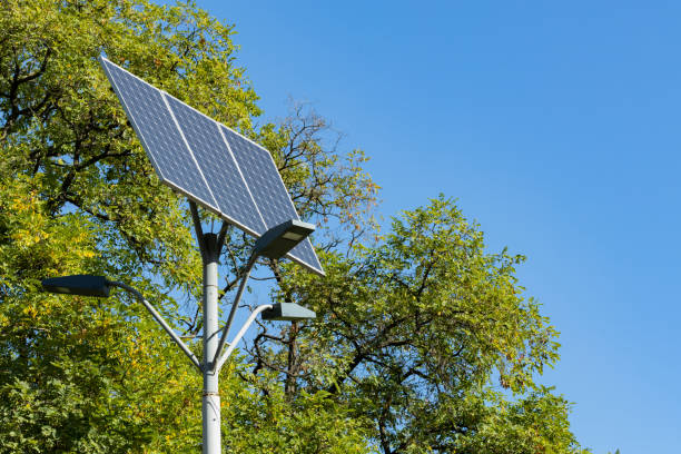 énergie solaire alternative. dispositif solaire avec le feu de rue sur le fond du ciel bleu et de l’arbre vert. lumière de rue alimentée par panneau solaire avec batterie incluse. espace de copie - nature sunlight tree illuminated photos et images de collection