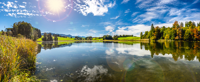 beautiful panoramic landscape in region Allgaeu, Bavaria, Germany with sun on sky over alps mountains nearby Forggensee lake in meadows