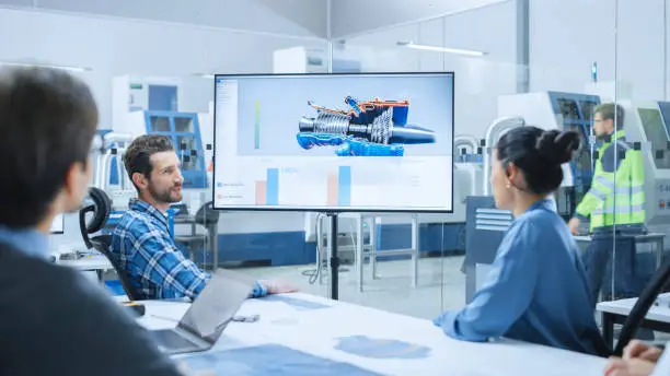 Modern Factory Office Meeting Room: Diverse Team of Engineers, Managers and Investors Talking at Conference Table, Watching Interactive TV that shows Sustainable and Renewable Green Energy Engine