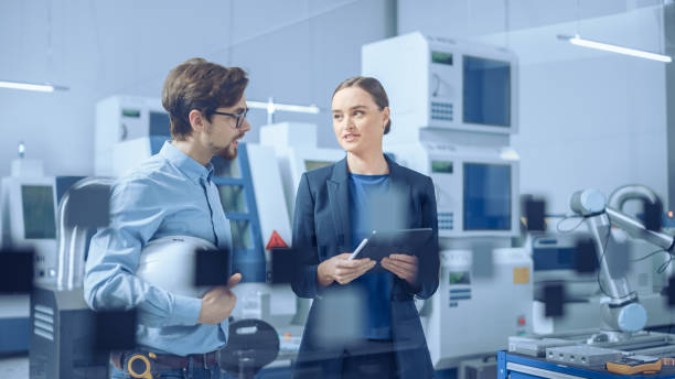 istock Modern Factory: Female Project Manager and Male Engineer Standing, Talking, Using Digital Tablet for Programming and Monitoring Assembly Line. Industry 4.0 Facility with High Tech Machinery 1282300401