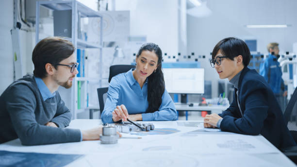 istock Diverse Team of Computer Engineers and Specialists Gather Around Conference Table, They Discuss Project Drafts, Find Problem Solutions. Electronic Factory. Office Meeting Room. 1282300487