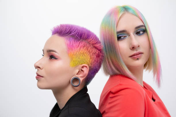 Young lesbian woman couple with vivd colored short hair and jackets posing on white background. Piercing on the face, tunnels in the ears. Young lesbian woman couple with vivd colored short hair and jackets posing on white background. Piercing on the face, tunnels in the ears. The concept of same-sex wedding. short human hair women little girls stock pictures, royalty-free photos & images