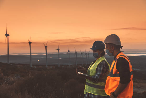 istock Maintenance engineer team with face mask working in wind turbine farm at sunset during pancemic 1282301717