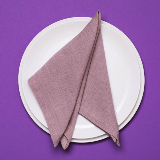istock Rolled up napkin in a plate on a purple background, top view 1282302630