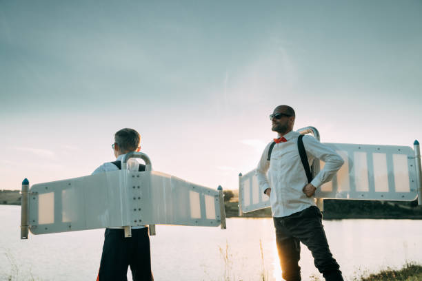istock Father and son wearing jetpack wings posing together. Sunny lakeshore 1282303119