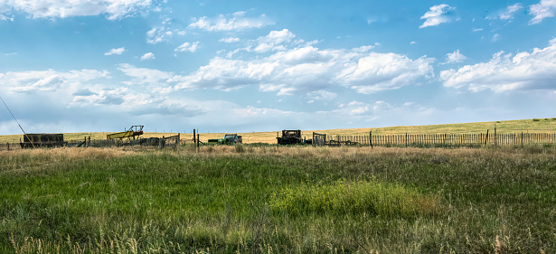 Brewster, Kansas, USA - June 25, 2020: Farm planted farm fields and old broken farm machinery - tractors and trucks - on the outskirts of Brewster in Kansas, USA. Traveling through America's summer countryside