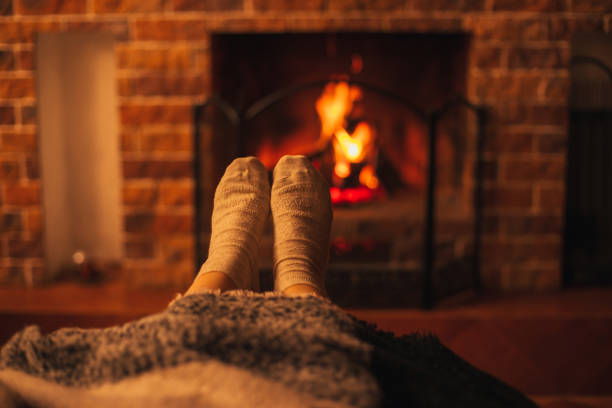 pieds femelles utilisant des chaussettes blanches s’asseyant près de la cheminée, enveloppant dans une couverture de laine. - blanket fireplace winter women photos et images de collection