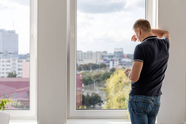 istock a man stands at a large window with a smartphone in his hand, view from the back 1282305882