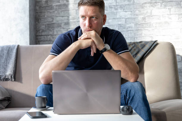 istock a pensive and serious middle-aged man sitting on a sofa with a laptop on a coffee table 1282305913