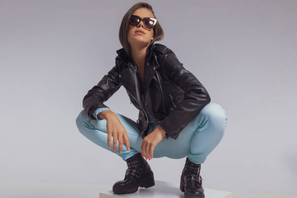 istock Charming fashion model wearing leather jacket and sunglasses, crouching 1282306762