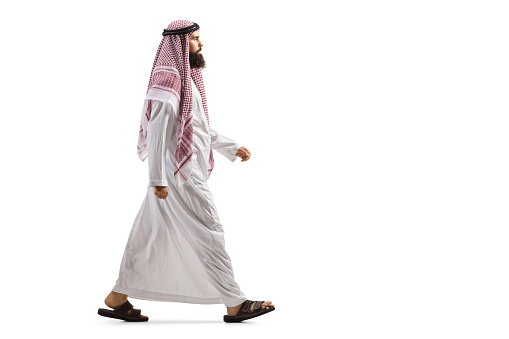Full length profile shot of an arab man in a traditional thobe walking isolated on white background