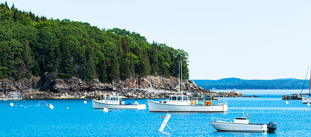 View looking at boats moored just off a rocky island in Bar Harbor Maine.
