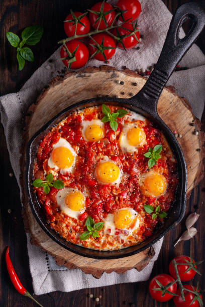 Fried eggs with tomatoes and vegetables. Shakshuka in a cast iron portioned pan on a wooden background top view. stock photo