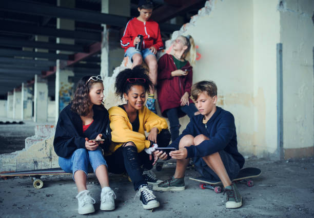 10代の若者のグループは、スマートフォンを使用して、放棄された建物の屋内に座ってギャング。 - youth culture gang member adolescence family ストックフォトと画像