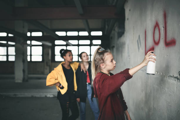 Group of teenagers girl gang indoors in abandoned building, using spray paint on wall. Group of teenagers girl gang standing indoors in abandoned building, using spray paint on wall. vandalism stock pictures, royalty-free photos & images