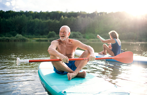 Active senior couple paddleboarding on lake in summer.