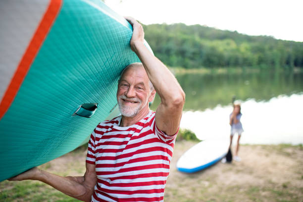 istock Senior man carrying paddleboard by lake in summer, looking at camera. 1282313023