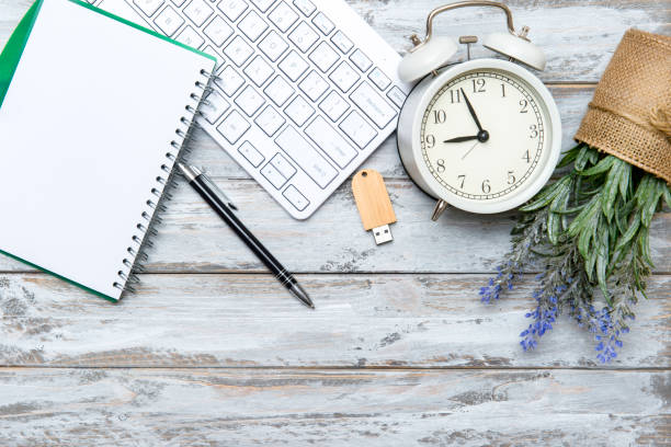 istock Home office workspace with computer keyboard, blank paper clipboard, alarm clock and green plant on wooden background. Flat lay, top view. Working home concept. 1282313190
