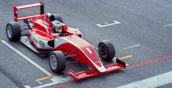 Racing driver in red uniform at starting line on track.