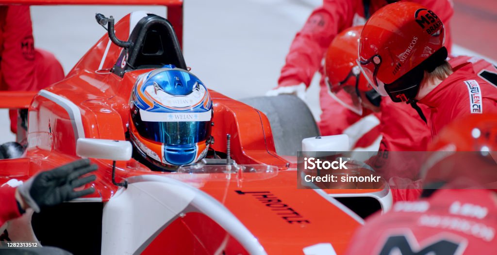 Pit crew working at pit stop Pit crew in red uniform changing tyres of open-wheel single-seater racing car car at pit stop. Race Car Driver Stock Photo