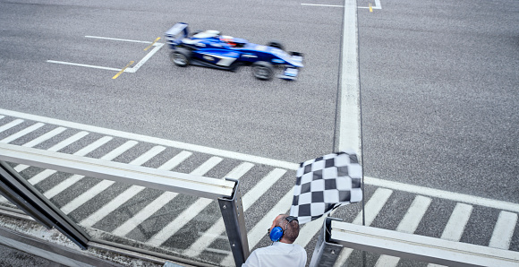 High angle view of auto race official waving chequered flag to blue open-wheel single-seater racing car car driving on track.