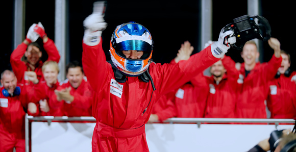 Portrait of open-wheel single-seater racing car car driver in red uniform raising his arms while celebrating his victory.