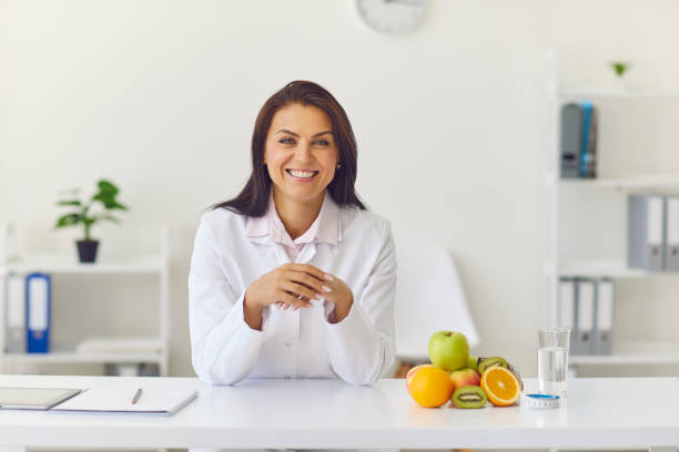nutricionista mulher feliz sentado em sua mesa no escritório olhando para a câmera e sorrindo - dietology - fotografias e filmes do acervo