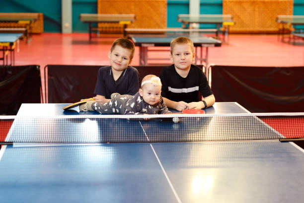 two boys and a little girl in table tennis are looking at the camera - tennis teenager little boys playing imagens e fotografias de stock