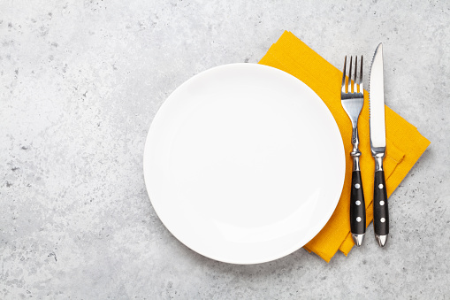 White empty plate, fork, knife and napkin on stone table. Top view flat lay with space for your meal