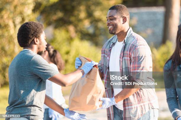 Food Bank Volunteer Hands Bag To Young Man In Need Stock Photo - Download Image Now - Giving Tuesday, A Helping Hand, Neighbor