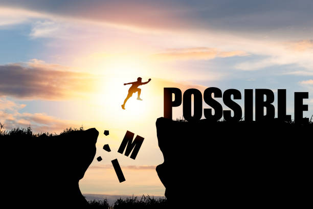 mindset concept ,silhouette man jumping over impossible and possible  wording on cliff with cloud sky and sunlight. - possible imagens e fotografias de stock