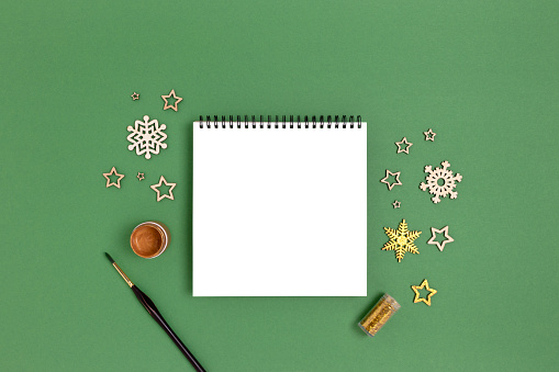 Clean notepad mockup with wooden New Years decoration and golden paint. Equipment for coloring Christmas toys on a green background.
