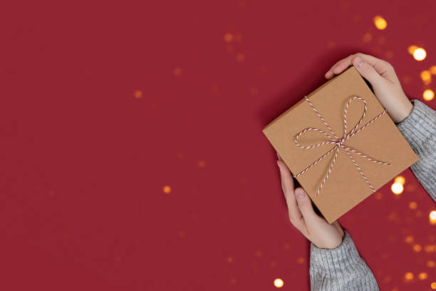 istock Hands hold gift box tied with rope on a red background. 1282322105
