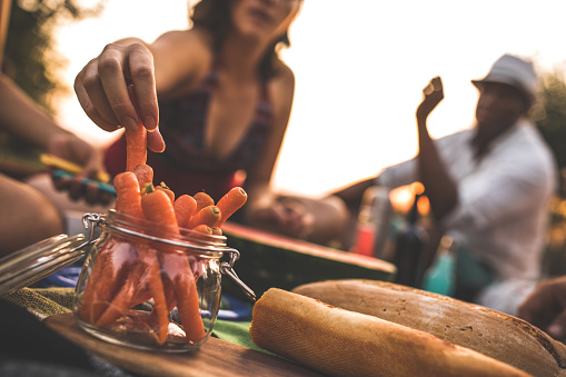 Close up, cut out of a baguette and a jar of orange thin carrots served for a picnic where a woman is choosing organic vegetables to eat.