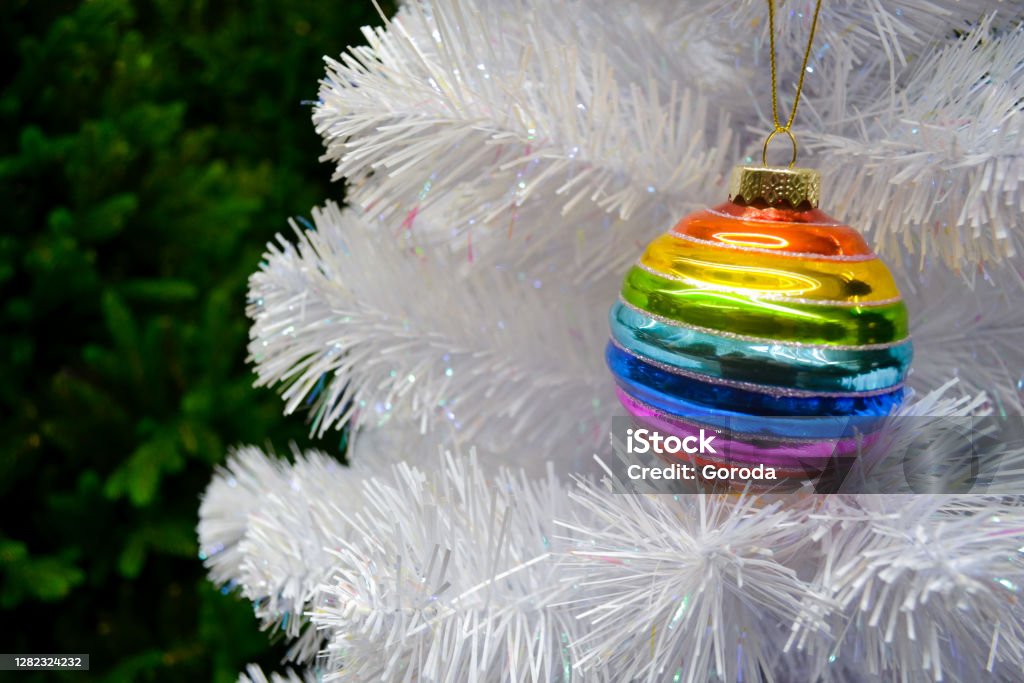 Bright Glass Rainbow Colored Christmas Ball Bauble Hanging On A White  Artificial Christmas Tree On Background Of Green Christmas Tree The Concept  Of Holiday Christmas Symbol Of The Rainbow Stock Photo -