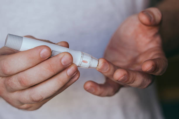 istock Close up of a man's hand using a lancet on his finger to check blood sugar using a glucose meter, using as medicine, diabetes, glycemia, healthcare and people concept. 1282324833