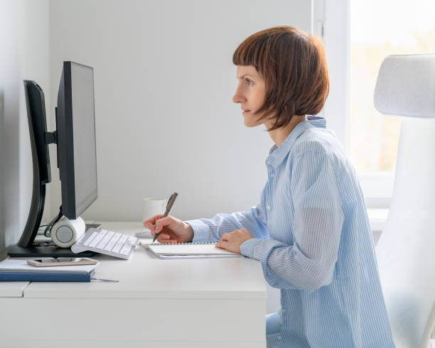 istock Mature woman looking at computer screen and writing information in notebook. Online course, Education. 1282326364