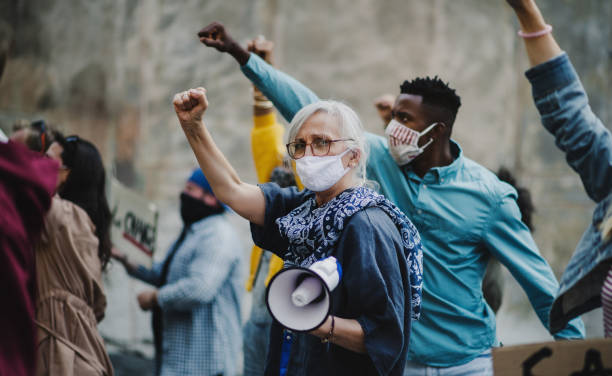 istock Group of people activists with raised fists protesting on streets, protests demonstration and coronavirus concept. 1282328376
