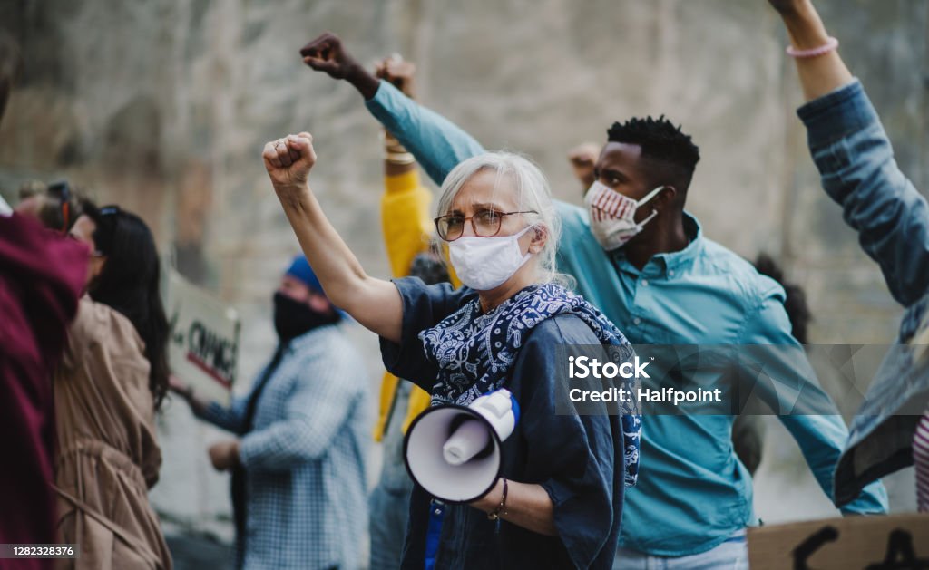 Group of people activists with raised fists protesting on streets, protests demonstration and coronavirus concept. Side view of group of people activists with raised fists protesting on streets, protests demonstration and coronavirus concept. Protest Stock Photo