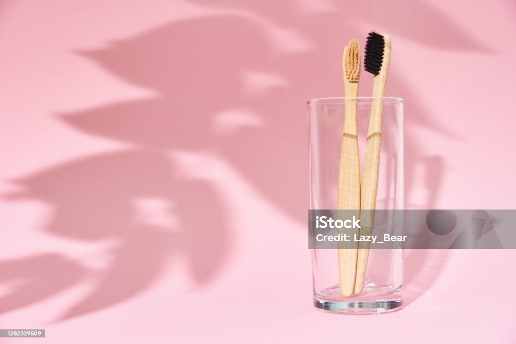 Bamboo toothbrushes in the glass and leaf shadows on pink background Bamboo toothbrushes in glass and leaf shadows on pink background Toothbrush Stock Photo