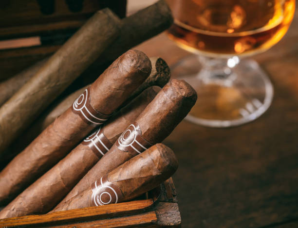 chiusura di sigari cubani su scrivania di legno, vetro sfocato di brandy - cigar whisky bar cognac foto e immagini stock