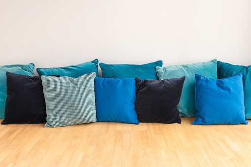 Tones of blue cushions stack on wooden couch with white wall.