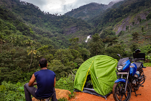 Mature motorcyclist sitting in front his tent in the morning and drinking coffee early in the morning